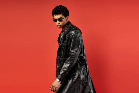 African American man in black trench coat on vibrant red backdrop.