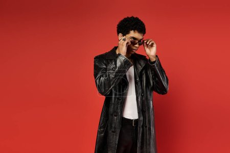 Téléchargez les photos : Beau Afro-Américain posant sur une toile de fond rouge frappante dans un élégant trench coat noir. - en image libre de droit