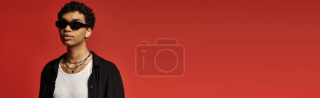 Photo for Stylish African American man wearing sunglasses, posing against vibrant red backdrop. - Royalty Free Image