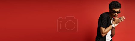 Photo for Handsome African American man in sunglasses poses against vibrant red backdrop. - Royalty Free Image