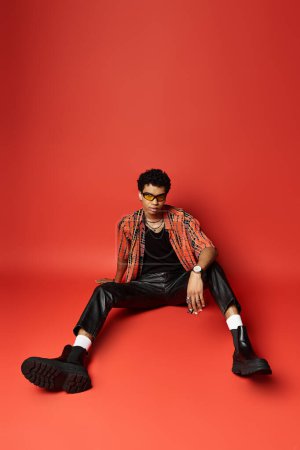 Photo for Handsome African American man sitting on floor in leather pants and red shirt. - Royalty Free Image
