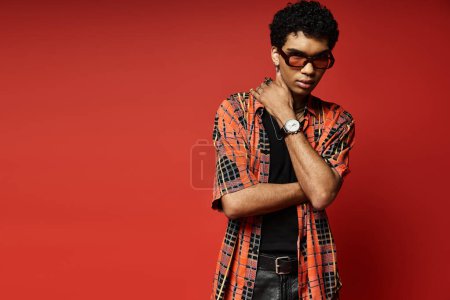 Hombre afroamericano guapo usando gafas de sol contra el fondo rojo audaz.