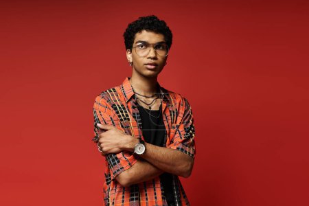 Handsome young man posing confidently in plaid shirt against vibrant red backdrop.