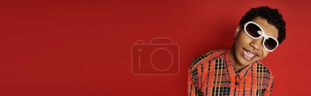 Handsome African American man wearing stylish sunglasses on red background.
