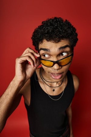A young man exudes cool vibes in sunglasses against a bold red backdrop.