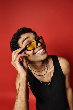 Handsome African American man wearing sunglasses on a bright red background.