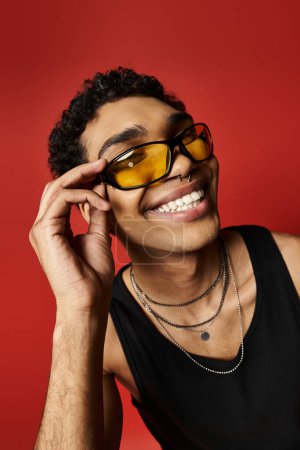 Téléchargez les photos : Beau Afro-Américain aux lunettes de soleil souriant sur fond rouge vif. - en image libre de droit