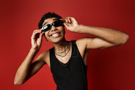 Foto de Un hombre afroamericano guapo luciendo gafas de sol de moda contra un telón de fondo rojo. - Imagen libre de derechos