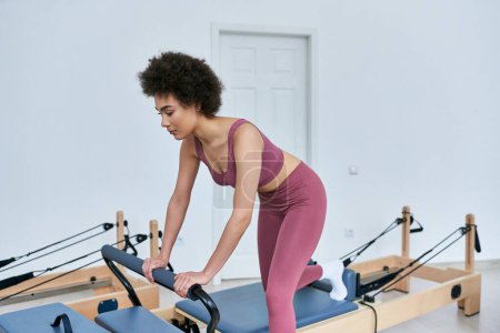 Une femme dans un top rose fait des exercices sur une rameur.