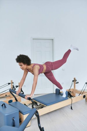 African American woman in pink, rowing machine workout.