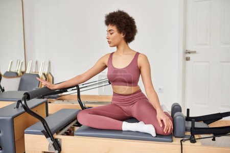 Woman practicing pilates seated on a mat in a peaceful class setting.