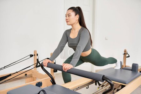 A sporty woman in gray shirt, green pants on Pilates lesson.