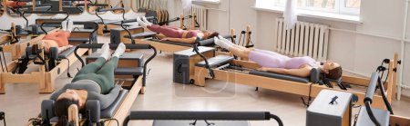 A diverse group of pretty sporty women, engaging in a pilates lesson on various exercise equipment.