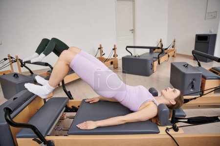 A sporty woman during a Pilates lesson in a gym, next to her friend.