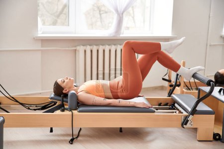 A sporty woman in an orange top engages in a pilates routine.
