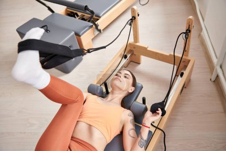 Eine sportliche Frau liegt während einer Pilates-Stunde auf einem stationären Trainingsgerät.