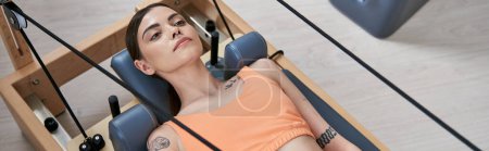 Photo for A sporty woman showcases her arm tattoo during a pilates lesson. - Royalty Free Image