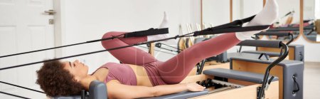 Eine sportliche Frau liegt während einer Pilates-Stunde elegant auf einem Fitnessgerät.