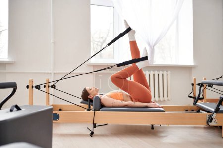 Téléchargez les photos : Fit femme effectue gracieusement des exercices lors d'une leçon de pilates. - en image libre de droit