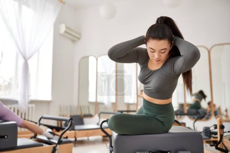 Asiatin in grauem Top und grüner Hose trainiert im Fitnessstudio neben ihrem Freund.