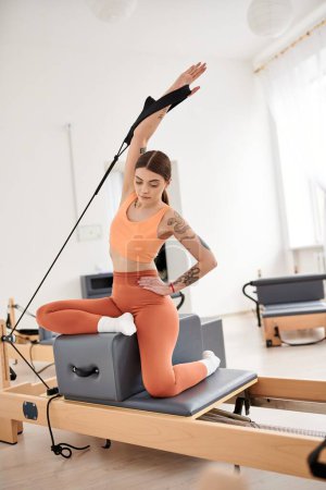 Foto de Una mujer deportiva con un top naranja y pantalones durante una lección de Pilates. - Imagen libre de derechos