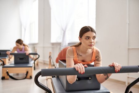A sporty woman exercising during a pilates lesson, next to her friend.