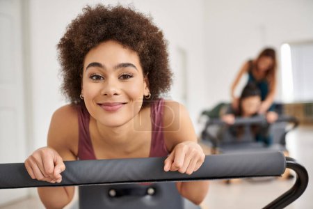 Sportlich fröhliche Frau beim Training während einer Pilates-Stunde, mit ihrem Freund im Hintergrund.