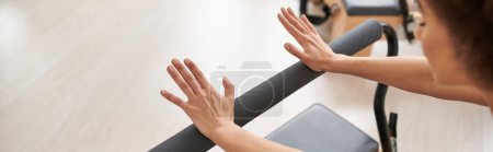 Photo for A sporty woman gracefully stretches her arms on a bar during a Pilates lesson. - Royalty Free Image