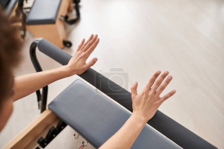 A pretty, sporty woman stretches her arms on equipment during a Pilates lesson.