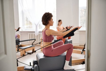 Téléchargez les photos : Bonnes femmes en tenue confortable pratiquant pilates dans une salle de gym ensemble. - en image libre de droit
