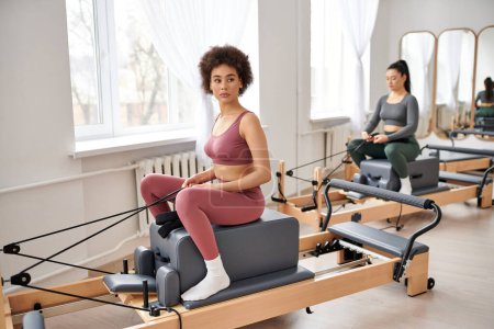 Attraktive Frauen in kuscheliger Kleidung üben gemeinsam Pilates im Fitnessstudio.