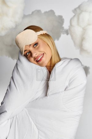 Beautiful dreamy woman covered in a white blanket surrounded by fluffy clouds.