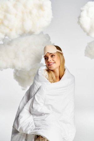 A dreamy blonde woman in cozy pyjamas smiles while wrapped in a blanket.