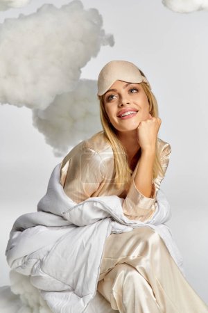 A dreamy blonde woman in cozy pyjamas sits gracefully atop a billowing cloud of smoke.