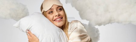Une femme blonde en pyjama confortable tient un oreiller au milieu des nuages.