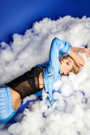 Una mujer de pelo rubio yace sobre una cama de nubes contra un cielo azul.