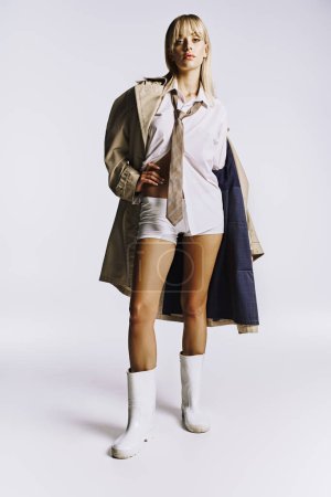 A stylish woman poses in short shorts and a trench coat against a white backdrop.