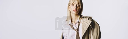 Photo for A stunning woman with blonde hair in a trench coat poses effortlessly against a white backdrop. - Royalty Free Image