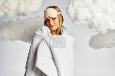 A beautiful blonde woman wrapped in a blanket, surrounded by fluffy clouds.