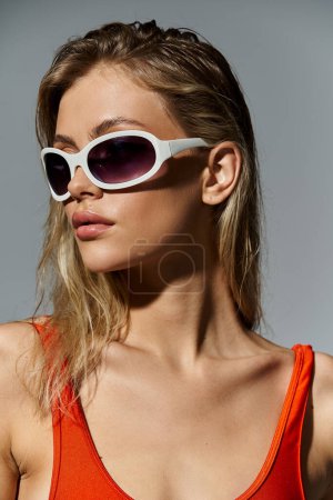 Mujer con estilo y cabello rubio con un top naranja y gafas de sol blancas.