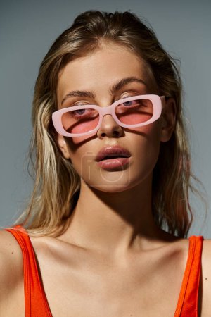 Foto de Una mujer con estilo en gafas de sol de color rosa y un top naranja emana un ambiente divertido y colorido de verano. - Imagen libre de derechos