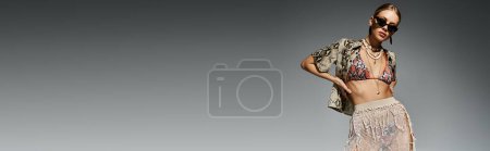 Téléchargez les photos : Femme blonde frappe une pose gracieuse dans un bikini élégant sur un simple fond gris. - en image libre de droit