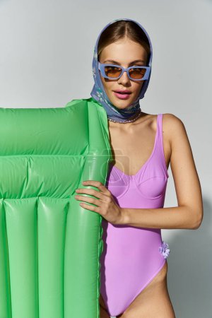 Foto de Fashionable blonde woman in purple swimsuit holding inflatable mattress. - Imagen libre de derechos