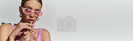 Foto de Mujer rubia con estilo disfrutando de una bebida a través de una paja en un traje de baño de moda. - Imagen libre de derechos