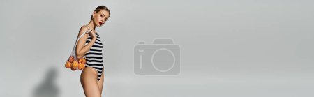 Téléchargez les photos : Femme blonde en maillot de bain rayé sur fond gris. - en image libre de droit