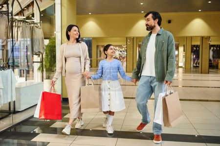 A happy family walks together in a shopping mall, carrying shopping bags filled with purchases.