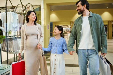 A happy pregnant woman and her daughter walk through a bustling shopping mall, enjoying family time and browsing stores.