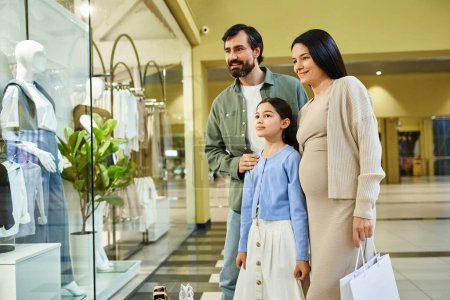 Téléchargez les photos : Une famille joyeuse parcourt les vêtements dans un centre commercial animé lors d'une sortie shopping amusante. - en image libre de droit