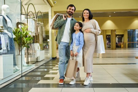 Eine glückliche Familie spaziert mit Einkaufstüten in der Hand durch ein Einkaufszentrum und genießt gemeinsam ein Wochenende der Einzelhandelstherapie.
