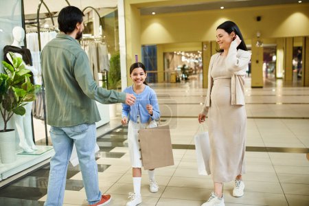 A man and woman shop with their daughter, enjoying a weekend outing at a bustling mall filled with shops and shoppers.